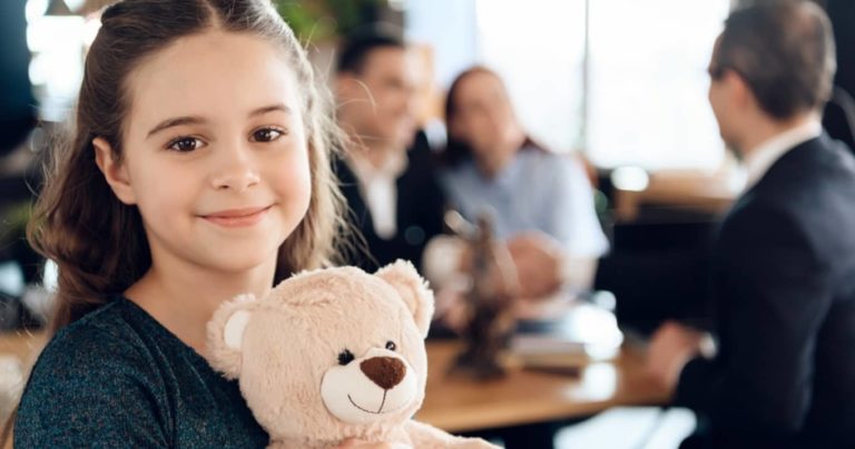 young girl holding a teddy bear stuffed toy with he parents at the background