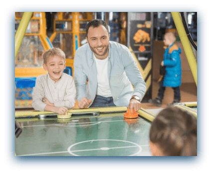 male parent playing air hockey with his kids in arcade