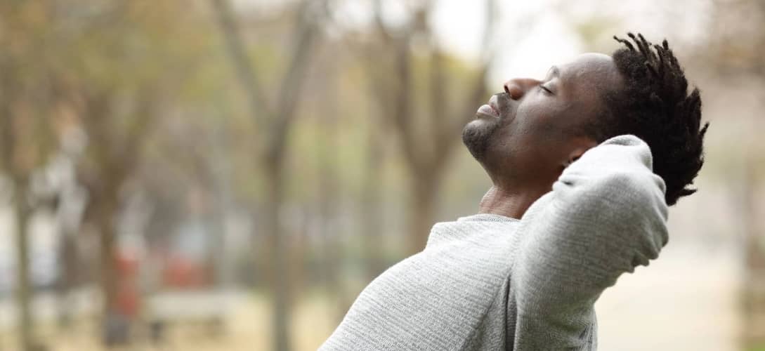 Side view portrait of a black man relaxing sitting on a bench in a park