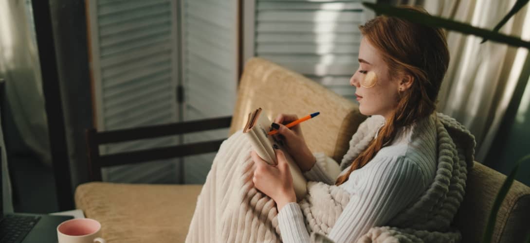 Cute lady with eyes patches at home writing notes on a diary while relaxing taking a break