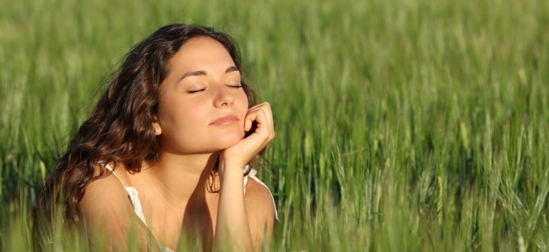 Woman breathing fresh air and relaxing in a green wheat field